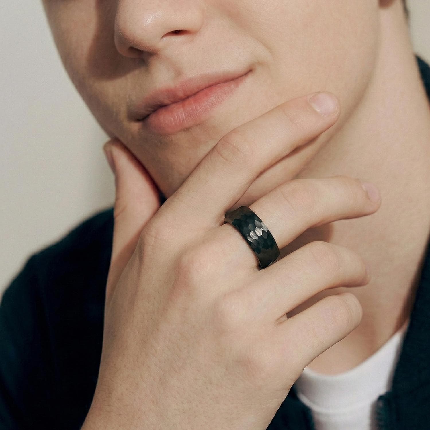 A close up of a man's face with his hand held up to his chin in a thoughtful pose. On his middle finger, he wears a black tungsten ring with a hammered effect.