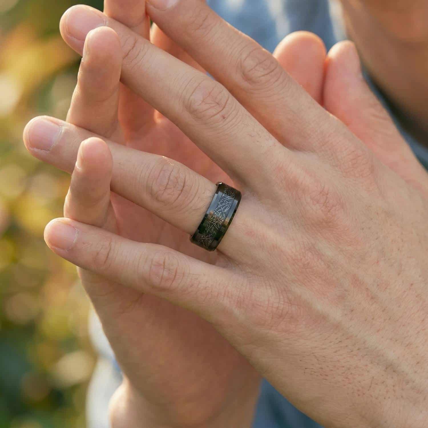 A close up of a pair of hands clasped together. On the mans hand is a black tungsten ring that has a centre section of faux meteorite.