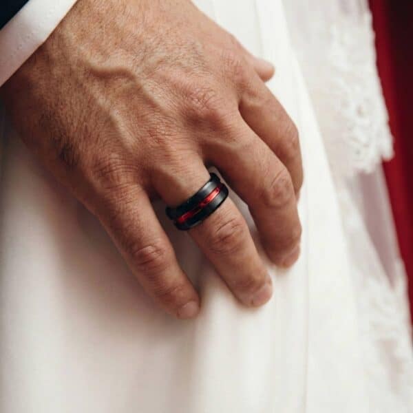 On the mans hand is a black and red tungsten ring. His hand rests against the bride's wedding dress.