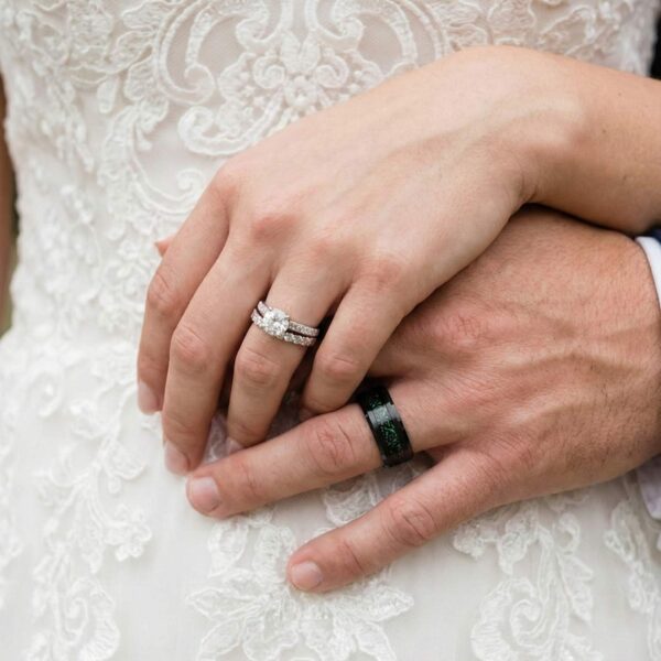 During the wedding ceremony, the couple embrace while holding hands, both showing their rings. The woman wears a silver ring studded with a diamond while the man wears a green and black ring made with carbon and tungsten.