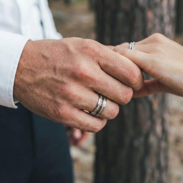 Holding hands as newly weds, the man is wearing a silver tungsten ring that has inlays of natural wood and antler.