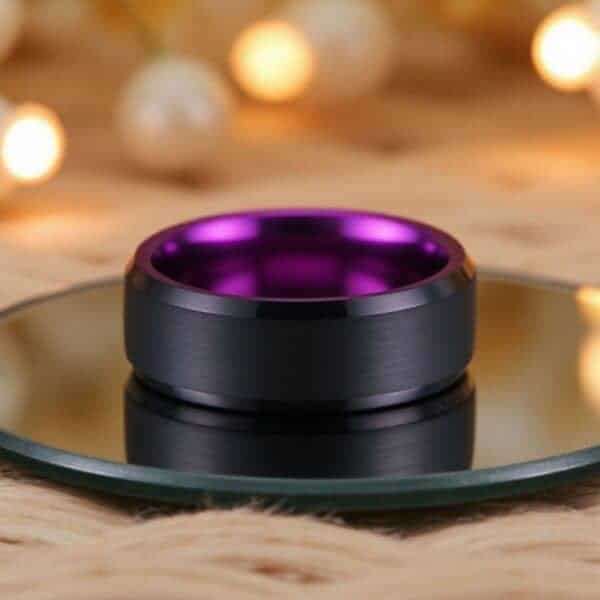 With fairy lights shimmering in the back of the image, there is a circular glass stand which has a ring laying on it. It is a black tungsten ring that has a purple inside.