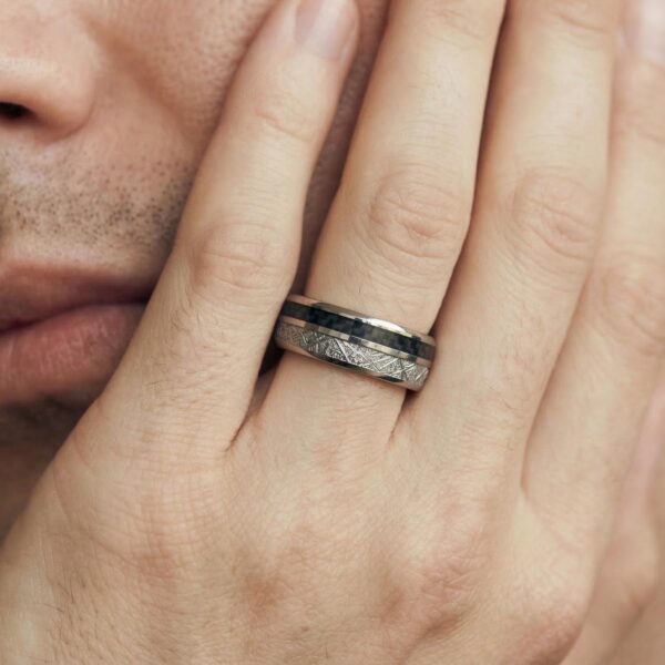 A close up image of a mans hand that he has held up to his face. He is wearing a distinctive ring. It is a silver tungsten ring that encompasses two distinct inlays - silver faux meteorite and black carbon fibre. Set within a domed silver tungsten ring.
