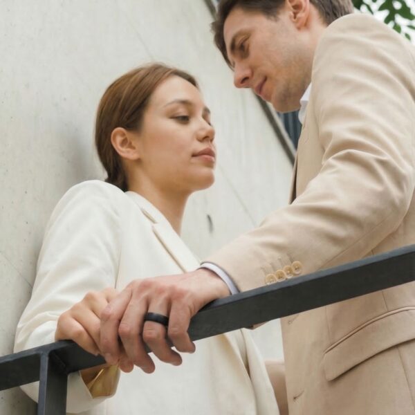 A couple have a quite moment together, holding on to the railings. The man is wearing a brushed black ceramic ring. Both are wearing cream coloured clothers.