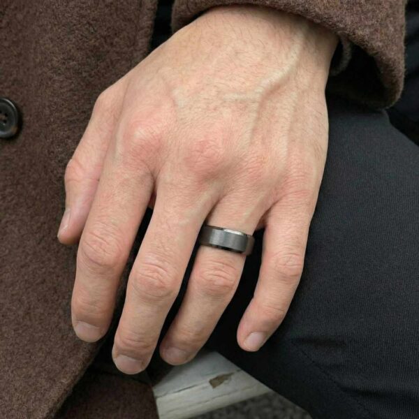 On the mans hand is a gunmetal grey tungsten ring - it has a brushed centre and polished bevelled edges.