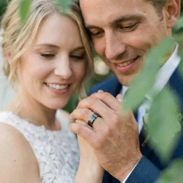 The romantic couple are newly weds. While the bride is wearing a traditional white bridal gown, the man shows that he is wearing a gunmetal grey tungsten ring on his wedding finger. The ring has a brushed finish at centre and polished bevelled edges.