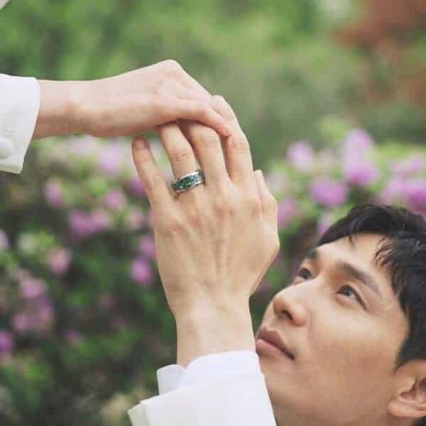 Among beautiful flower gardens, a man kneels down to take the hand of his partner. On his hand, he is wearing a silver tungsten ring. The multi faceted bevelled edges catch the light from all angles. The ring features a striking abalone shell inlay.