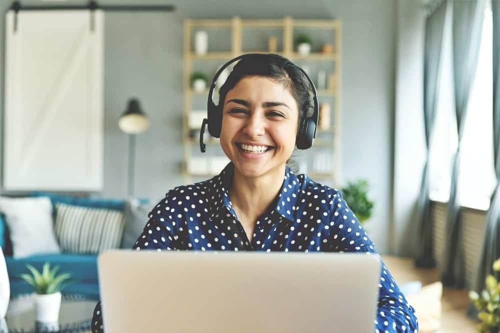 Happy indian woman professional tutor educating client online. Head shot cheerful smiling pretty hindu ethnic girl sitting at table with computer, wearing headphones with mic, looking at camera