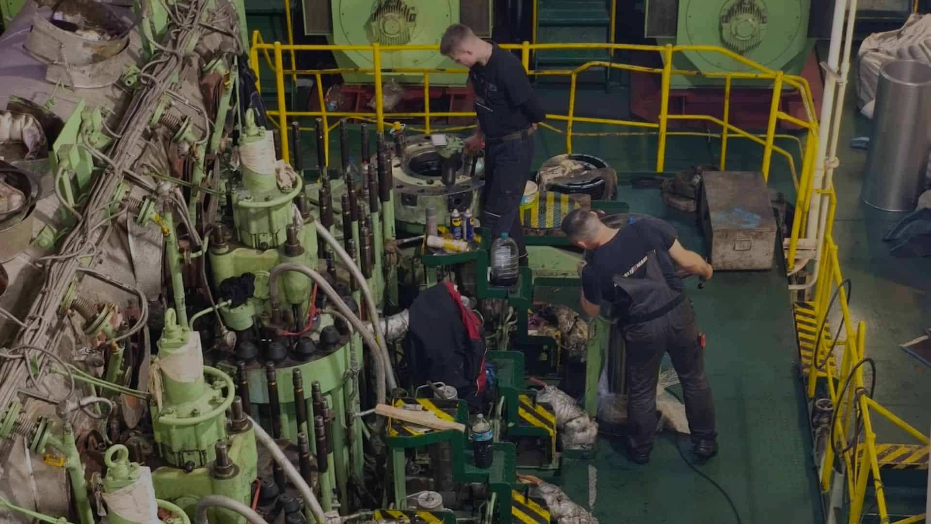 Two engineers working on marine machinery onboard a vessel.