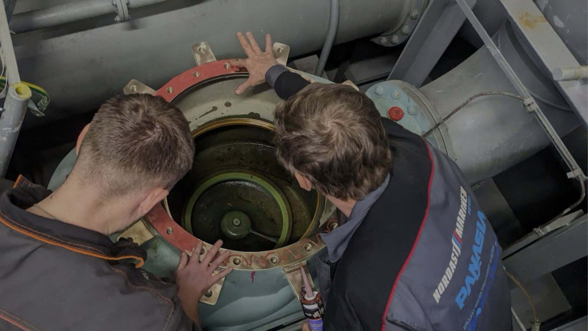 Two engineers inspecting a ship's machinery opening.