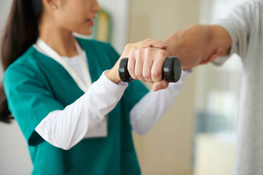 Physical therapist assisting with arm exercise using dumbbell.