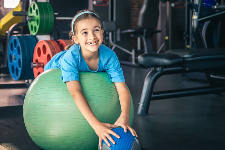 Young girl doing pediatric therapy with exercise ball at gym.