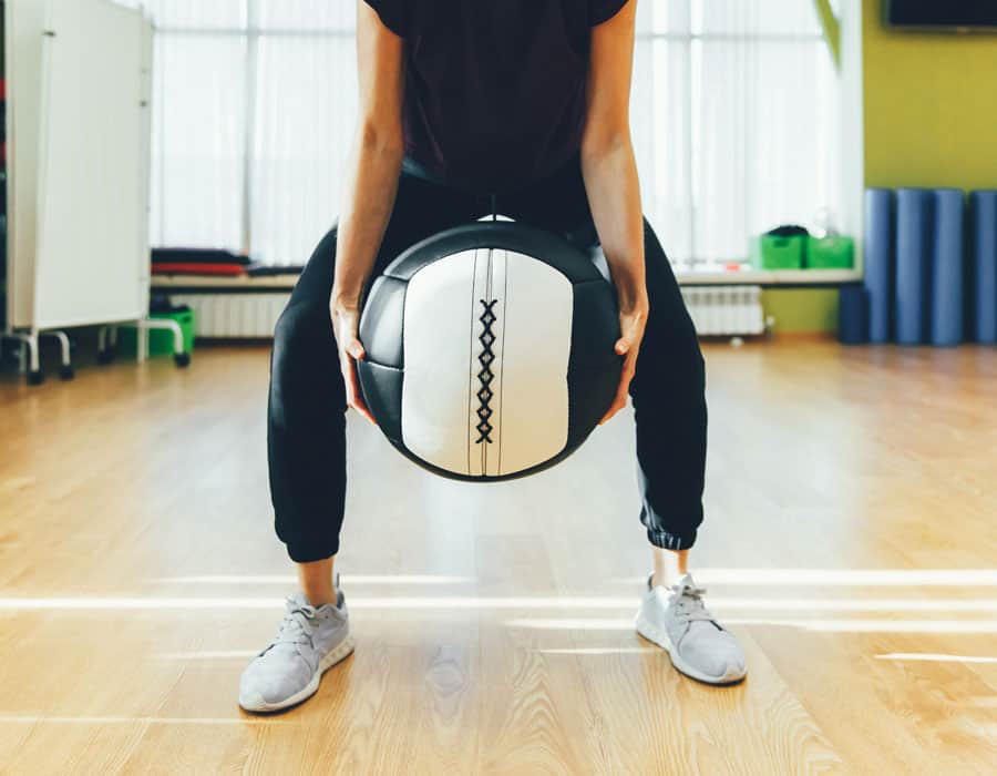 Person holding a medicine ball during physical therapy exercise in gym.