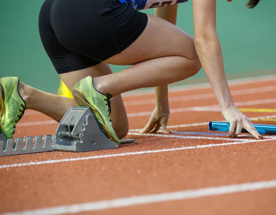 Athlete preparing for race on indoor track with starting blocks.