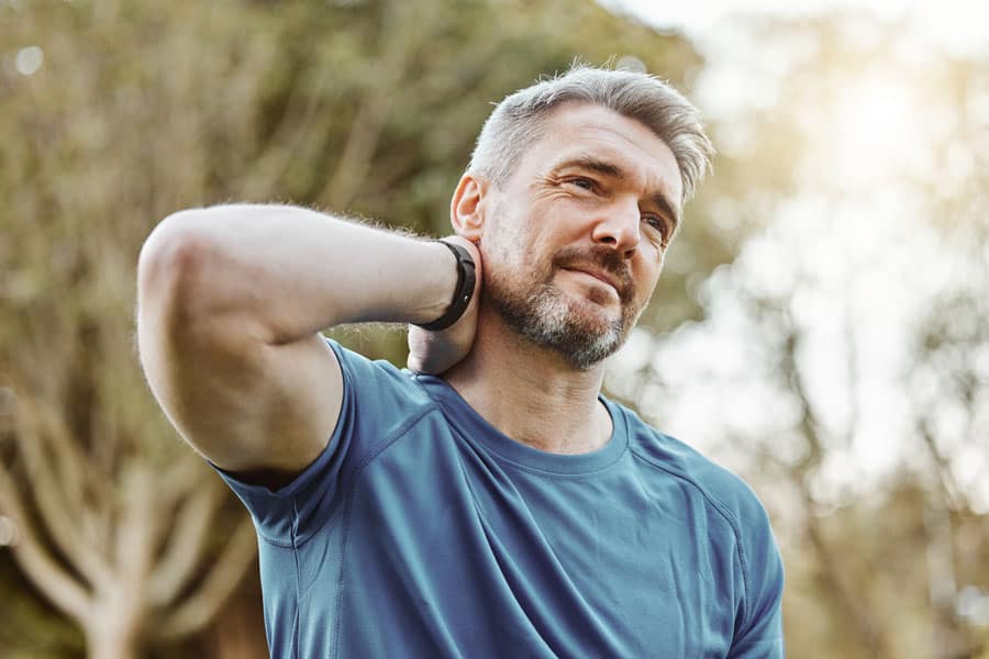 Middle-aged man stretching neck outdoors for pain relief.