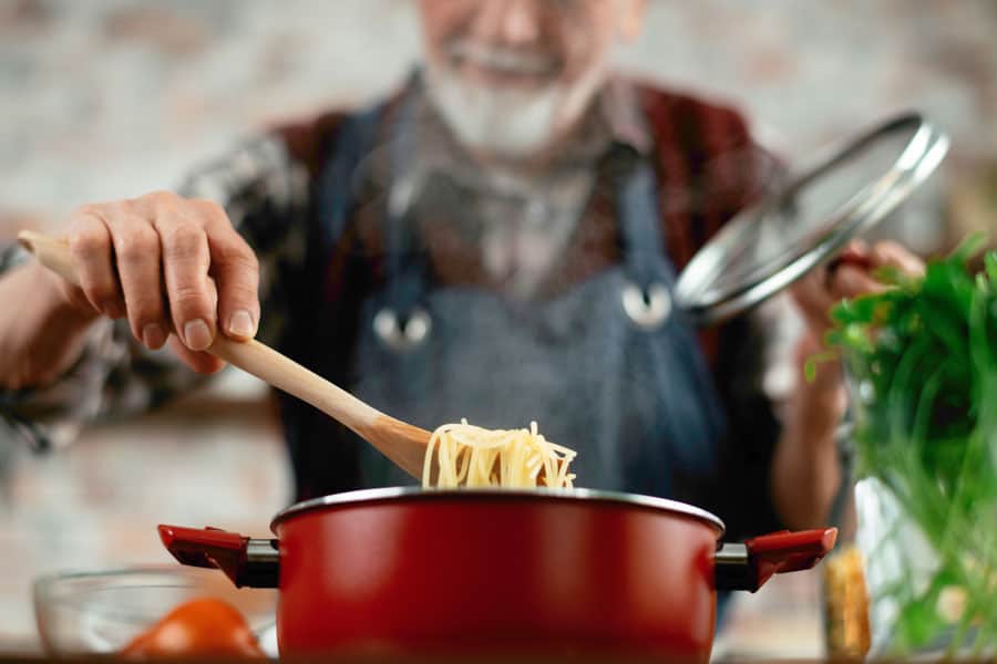 Elderly man enjoying cooking therapy with pasta in a red pot.