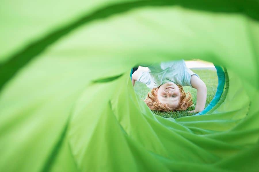 Child lying inside a green sensory play tunnel for sensory integration therapy.