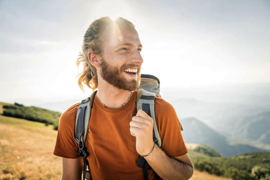 Smiling man with backpack enjoying outdoor hike in scenic landscape.