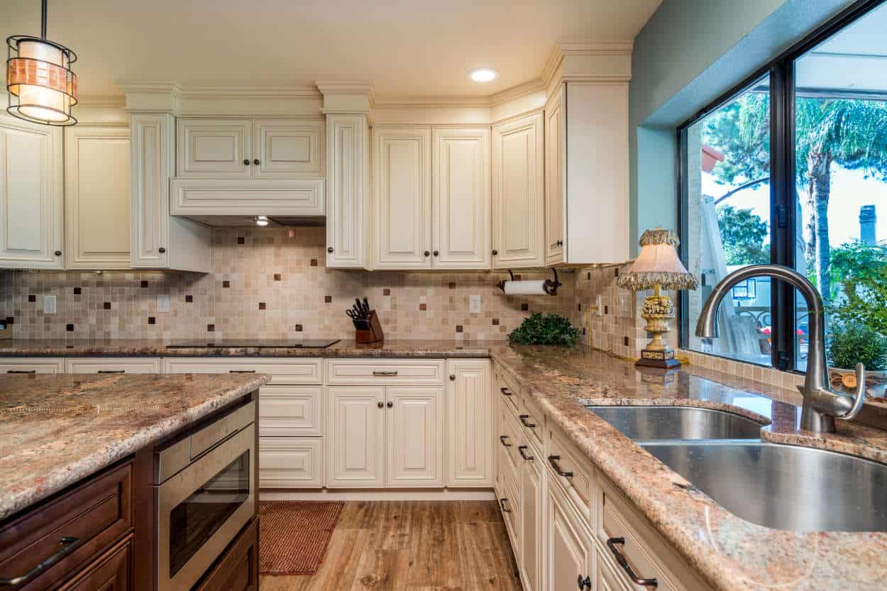 Brown and cream kitchen with wood flooring, granite countertops, and tiled backsplash.
