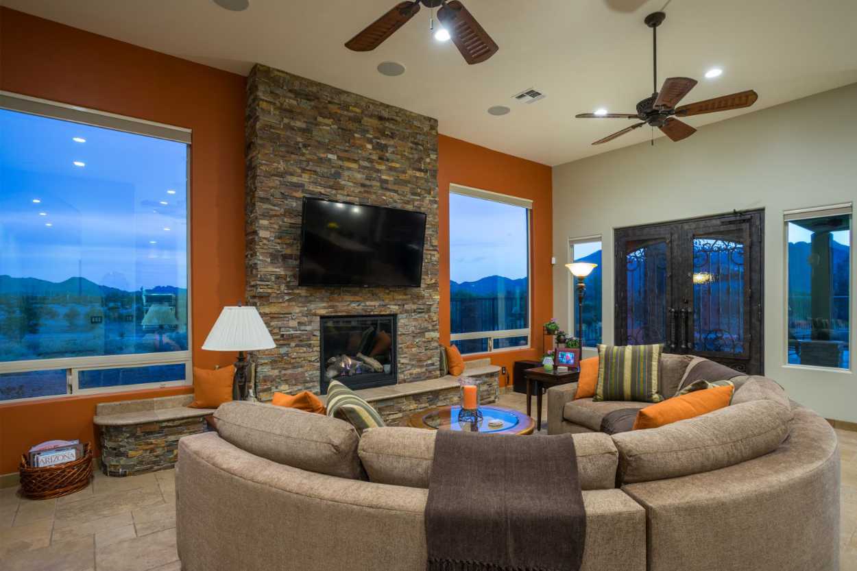 Living room with orange and gray walls, floor-to-ceiling brick wall with fireplace, and large windows.
