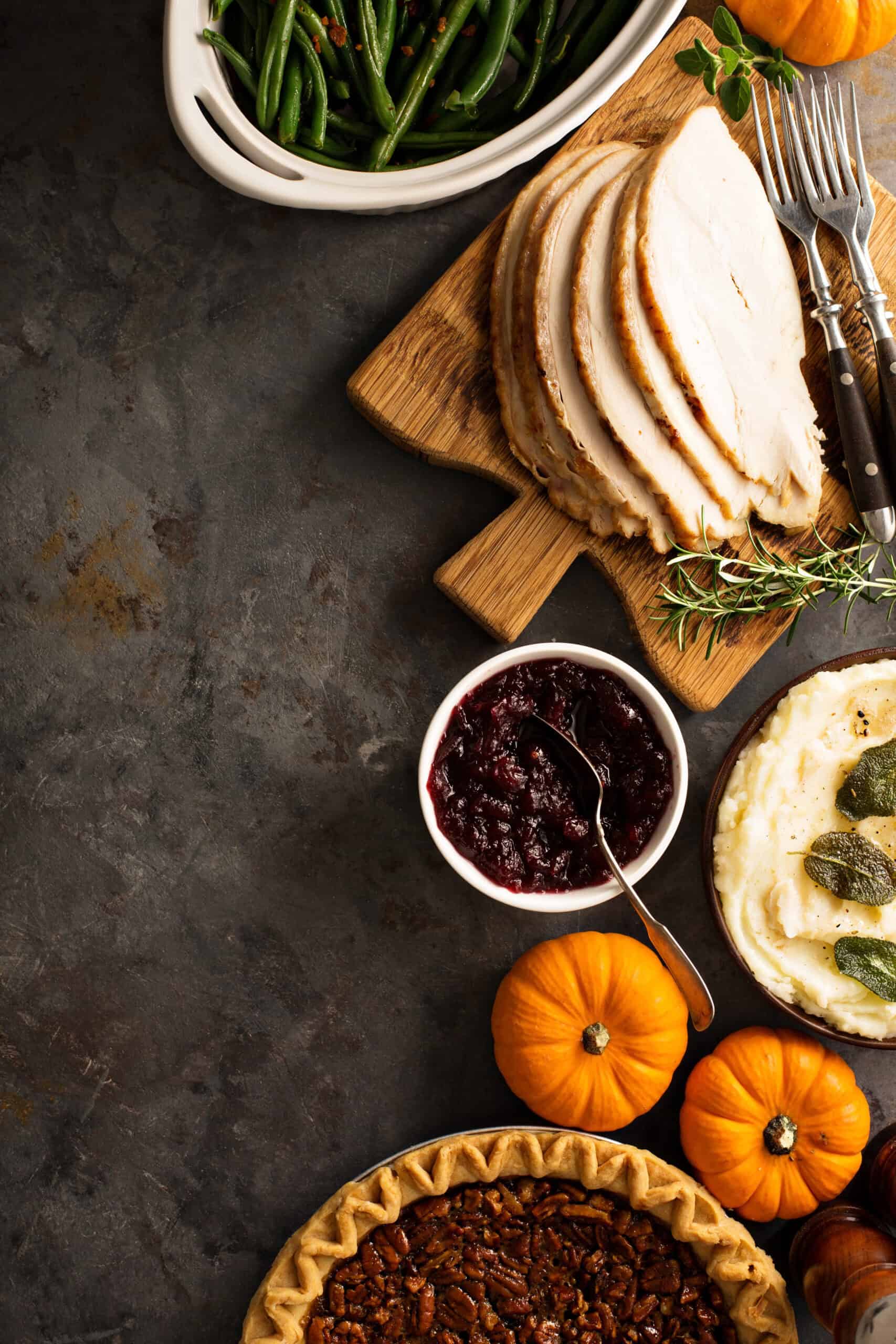 Thanksgiving meal featuring sliced turkey on a wooden board, green beans, mashed potatoes with sage, cranberry sauce, and pecan pie—just as America’s Founders might have enjoyed—with small pumpkins, forks, and herbs on a dark table.