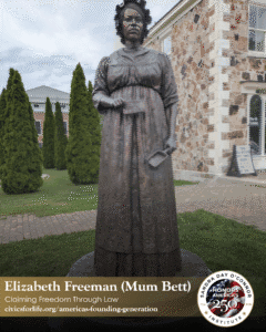 A bronze statue of Elizabeth Freeman (Mum Bett), known as The Citizen, stands outdoors on a brick walkway, with tall green shrubs and a stone building with large windows in the background.