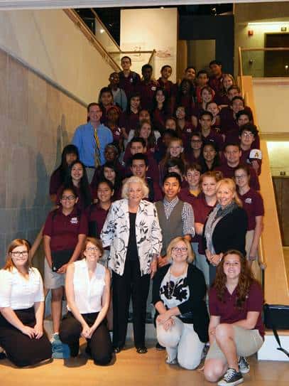 A large group of students in maroon shirts and khaki bottoms, along with several adults, pose for a photo on a staircase, gathering to celebrate their shared commitment to justice inside the building.