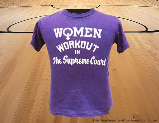 A purple t-shirt with the text "Women Workout in the Supreme Court" printed in white. The background shows a basketball court with wooden flooring.
