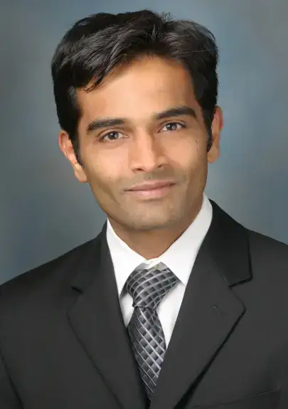A professional male doctor in a suit, smiling confidently against a neutral background, representing oncology and cancer treatment expertise.