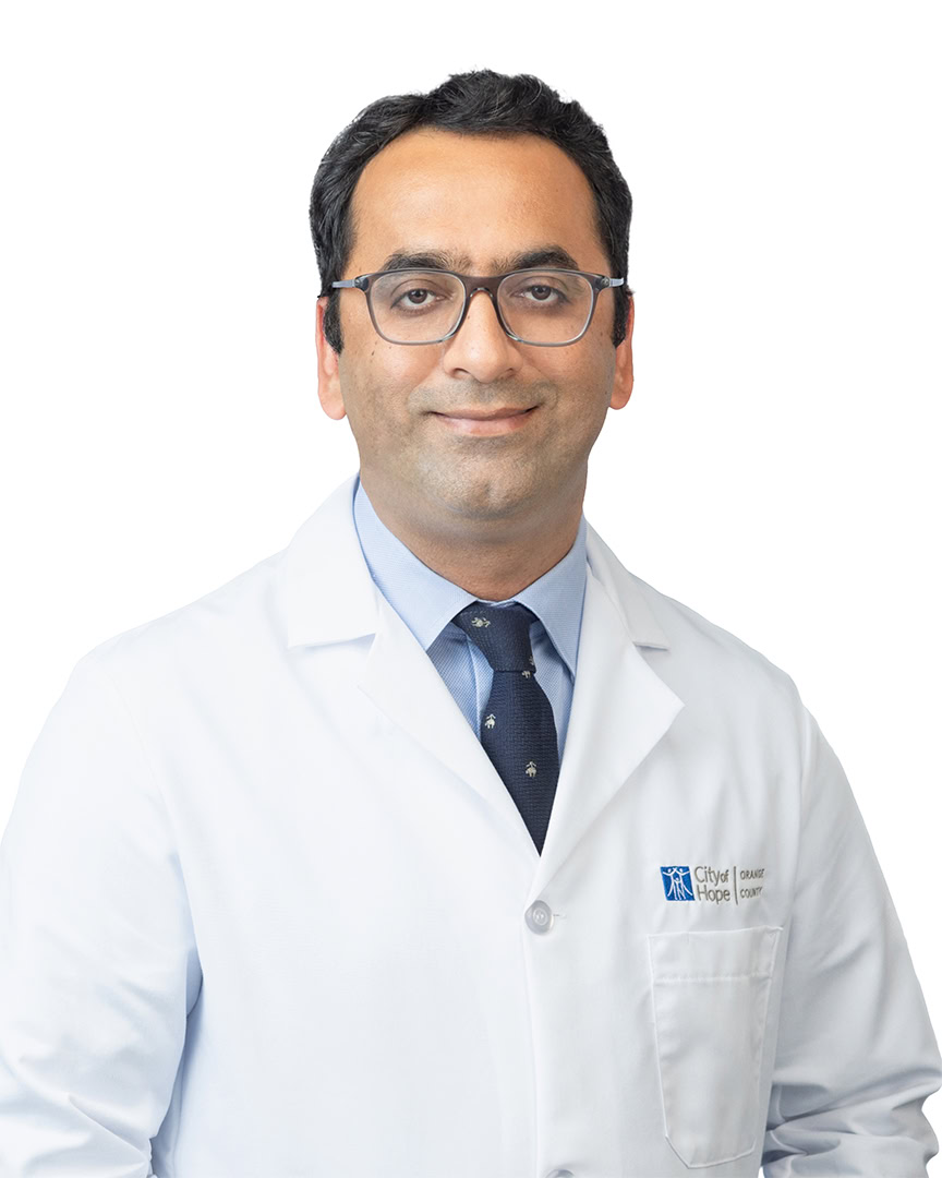 Male medical professional in white lab coat, eyeglasses, and blue shirt with tie, standing against white background, representing healthcare, oncology care, and medical expertise.
