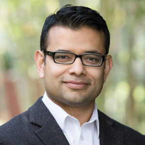 A confident professional man outdoors, wearing glasses and a business suit, representing medical or healthcare expertise for Oncology updates.