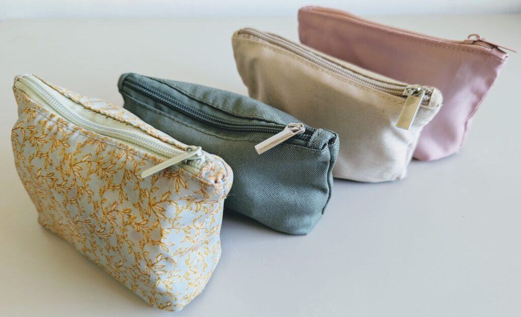 Set of four compact travel pouches arranged left to right: toiletries (floral), tech (green), miscellaneous items like first aid and laundry sheets (beige), and international travel accessories such as passport, currency and adapters (pink). Part of the minimalist carry-on packing system from One Small Bag.