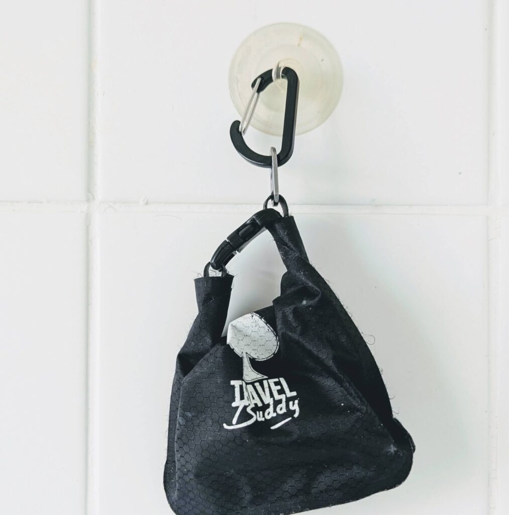 Lightweight Travel Buddy dry bag hanging in a tiled shower — the perfect waterproof pouch for solid toiletries on the go.