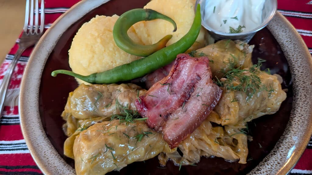 Romanian food at Ceasu' Rău - Sarmale with mămăligă (polenta), a green pepper, and a pot of sour cream (smântână)