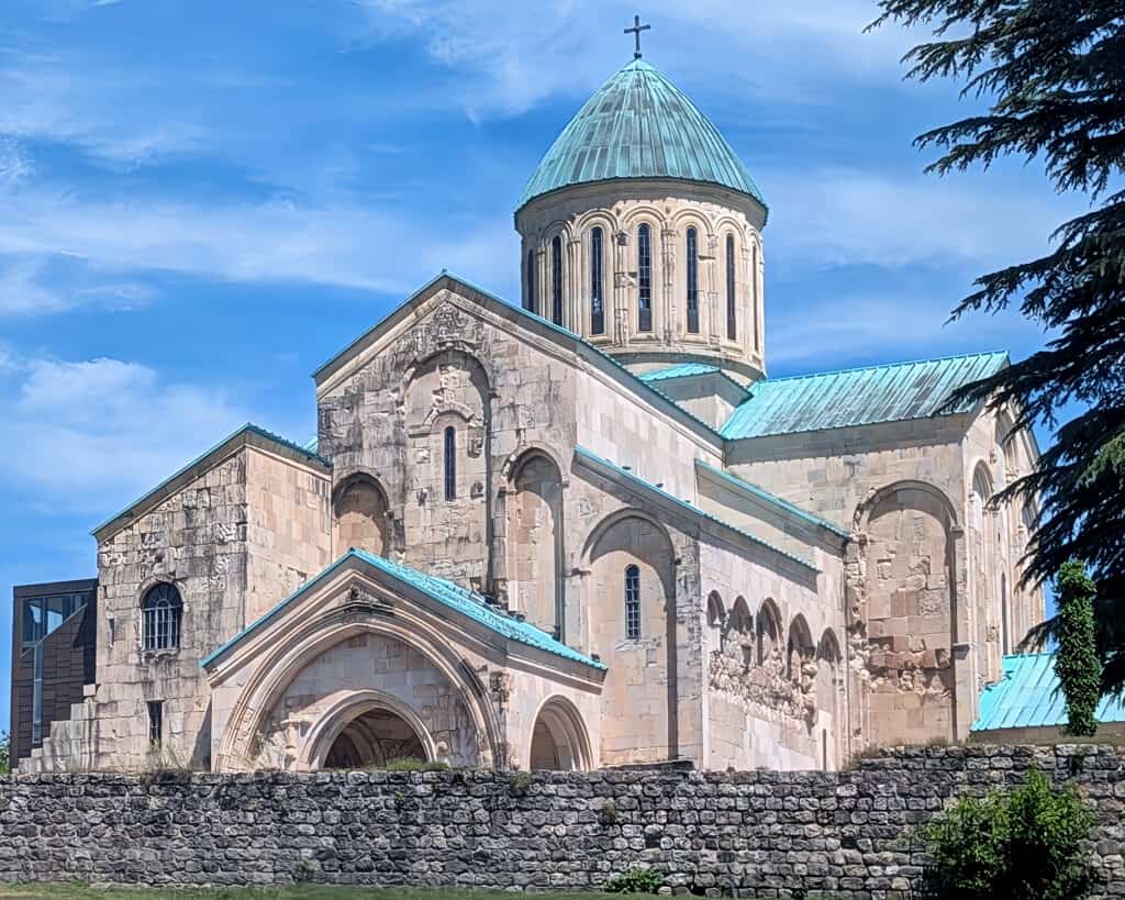 Outside of Bagrati Cathedral in Kutaisi - view from the front = blue green roof and domes and intricate carved white / cream stone. A visit is one of the top things to do in Kutaisi
