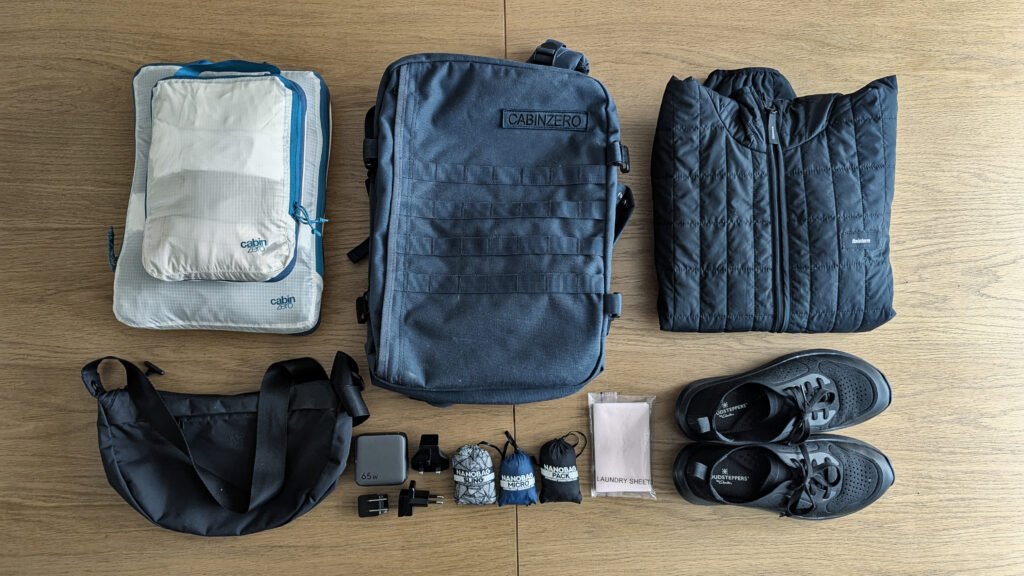 8 Travel Essentials in One Small Underseat bag- Flatlay - Cabin Zero military Bag - Moonbag - packing cubes - tech Jacket - ultralight shoes - Nanobags - wall charger - laundry sheets