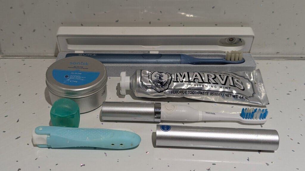 Travel Toiletries flat lay - Dental Care - Suri Electric toothbrush, Sonisk battery toothbrush, folding toothbrush, Marvis teeth whitening toothpaste and Sonisk teeth whitening powder
