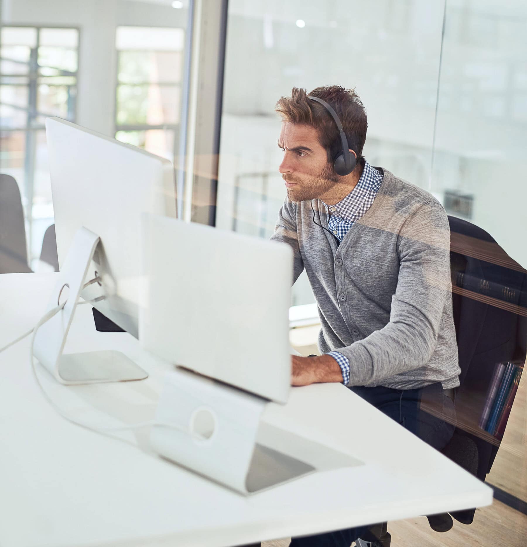 Man working at computer with headphones in office environment.