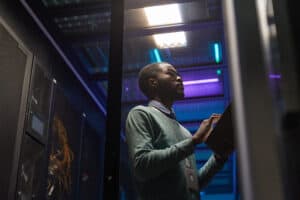 Man working in a data center with server racks and blue lighting.