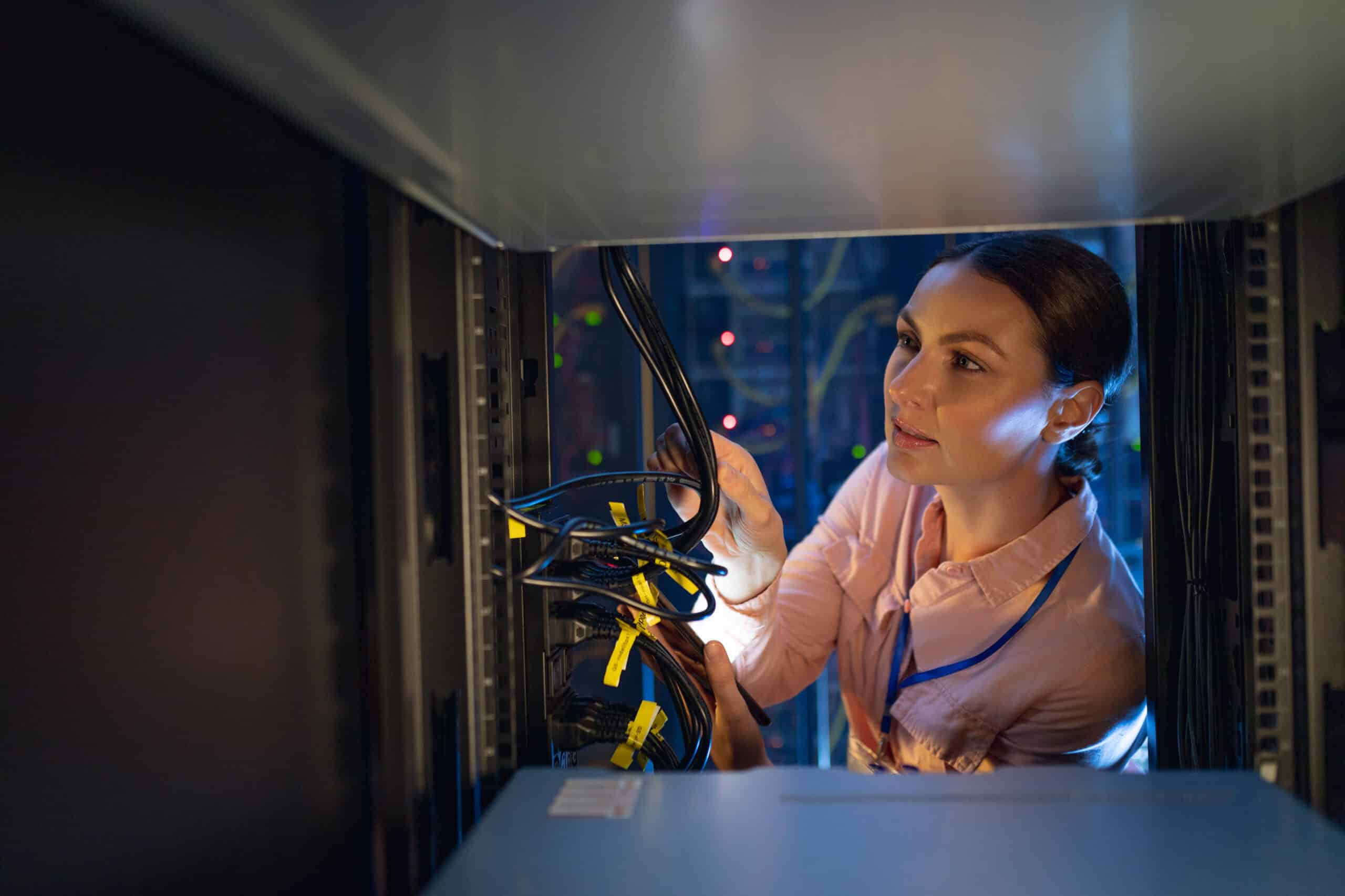 Female technician working inside a server room with network cables and equipment.