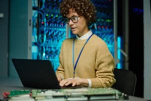 Female technician working on a laptop in a server room.