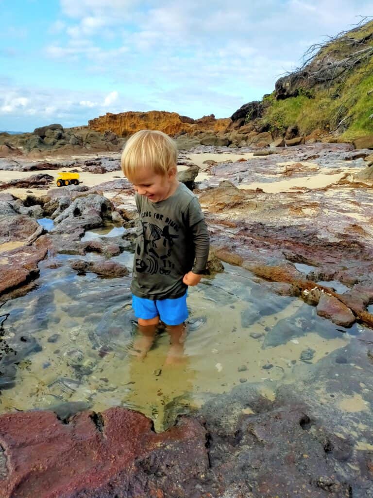 Child playing in tide pool at rocky beach.