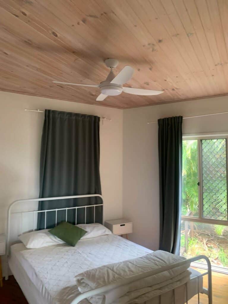 Bedroom with white bed, green pillow, and large window with curtains.