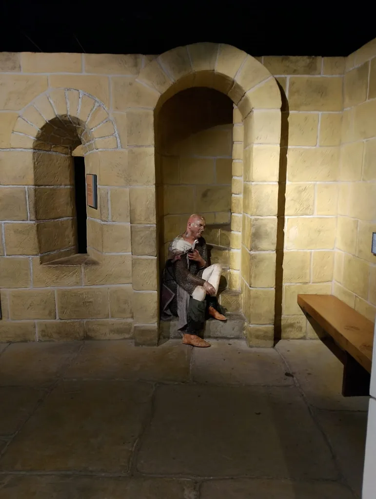 Intricately carved stone castle wall with a statue of a medieval man sitting on a step, showcasing detailed craftsmanship in an exhibition or museum setting.