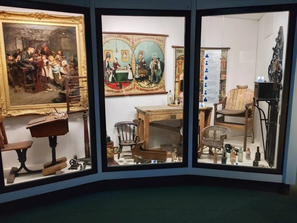 Vintage toy collection in glass showcase including dolls, bottles, and wooden furniture.