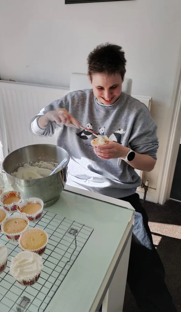 A young person decorating cupcakes with icing at a kitchen table.
