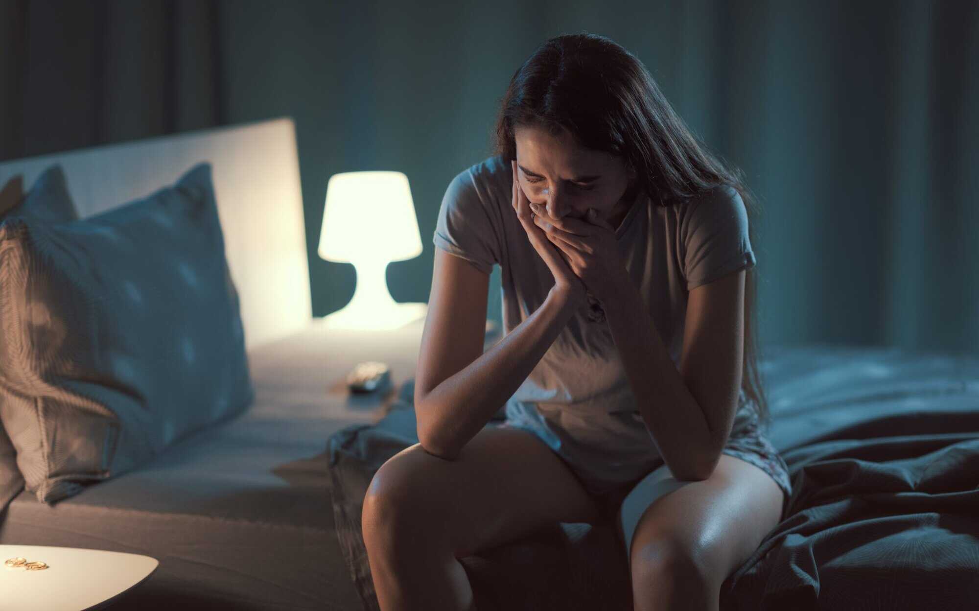 Woman experiencing tooth pain at night in a dark bedroom.