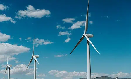 Two white wind turbines under a bright blue sky with scattered clouds.