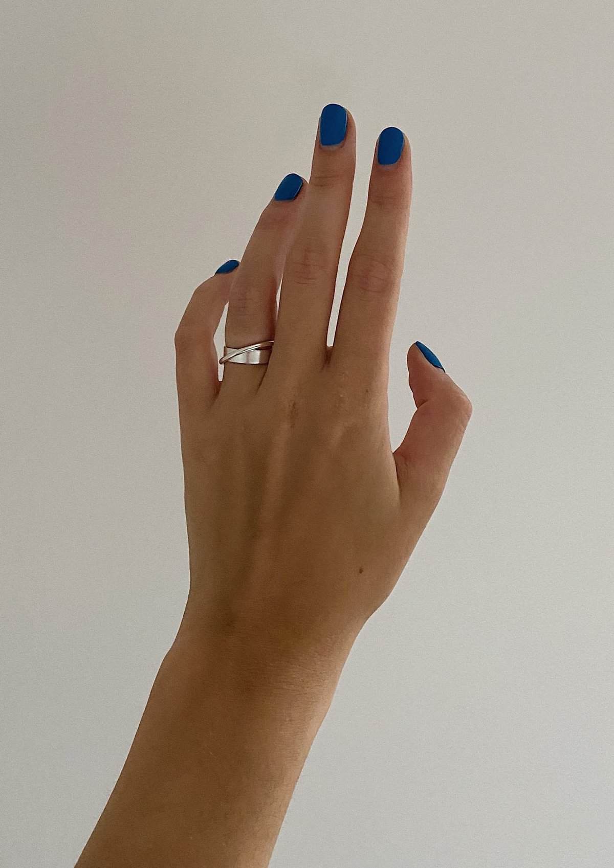 Silver Andromeda ring on a woman's finger with blue nail polish.