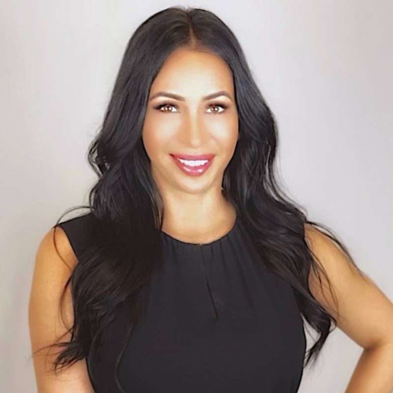 Woman with long dark hair wearing a black sleeveless top, smiling confidently at the camera.